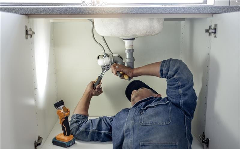 Plumber repairing pipes beneath a bathroom sink in Escondido