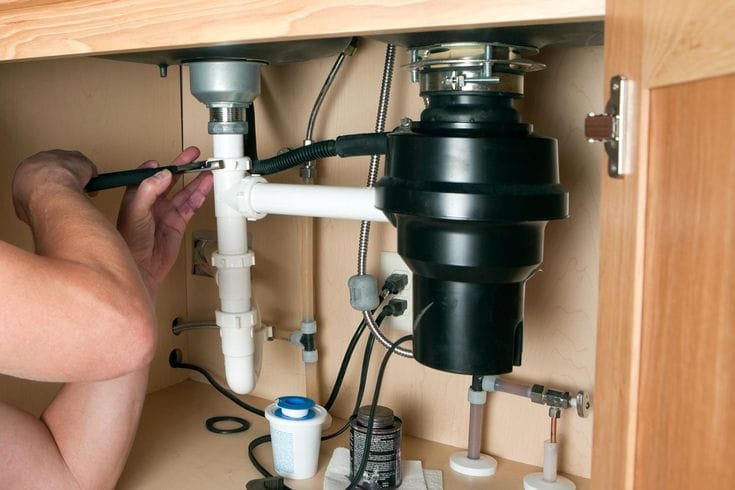 Plumber installing a garbage disposal beneath a kitchen sink in Escondido
