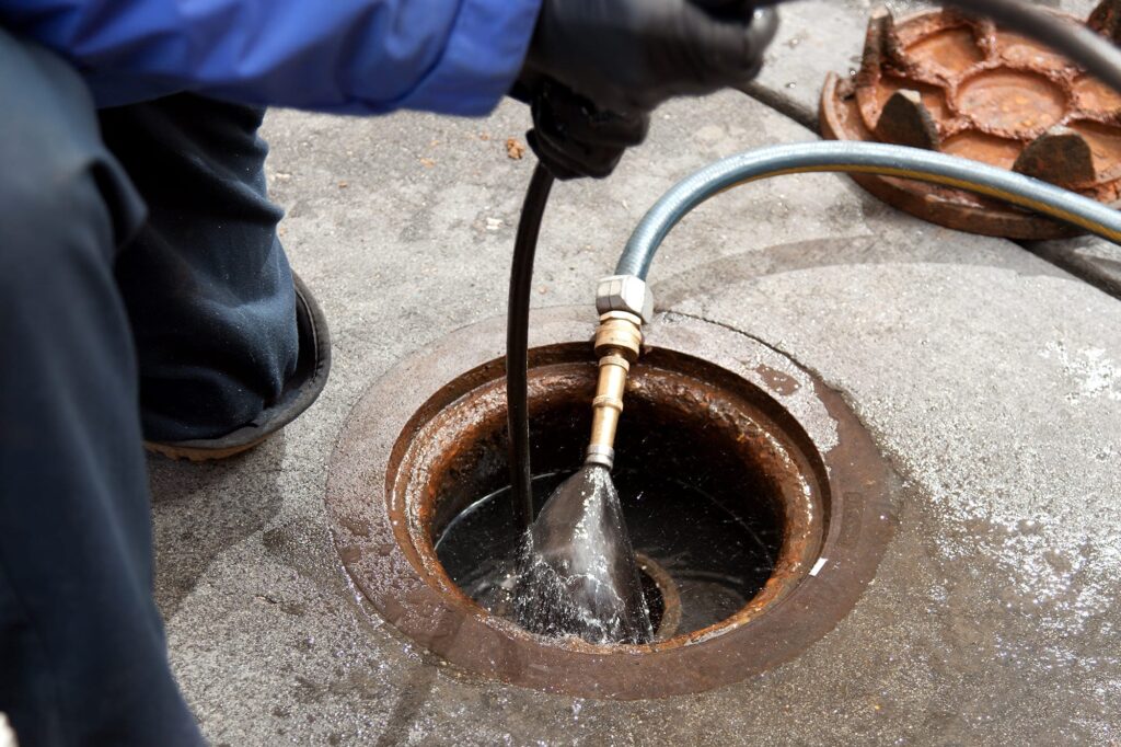 Plumber hydro jetting a sewer line through a manhole in Escondido